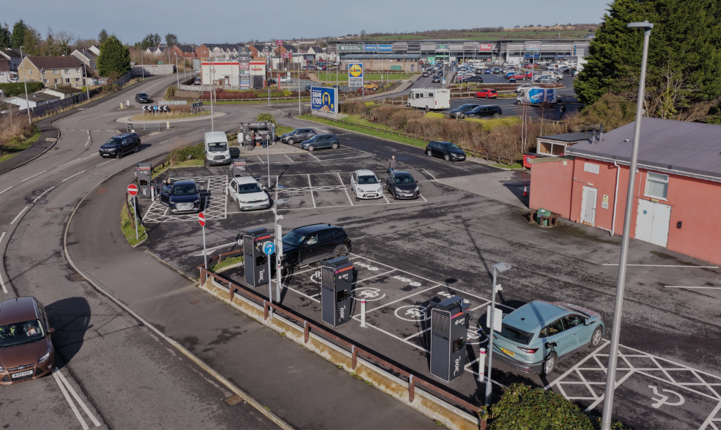 Aerial view of the Cross Hands EV charging hub — Alpitronic 300 kW chargers in use at Maes Yr Eithin Retail Park, with Aldi, Lidl and Costa visible in the background
