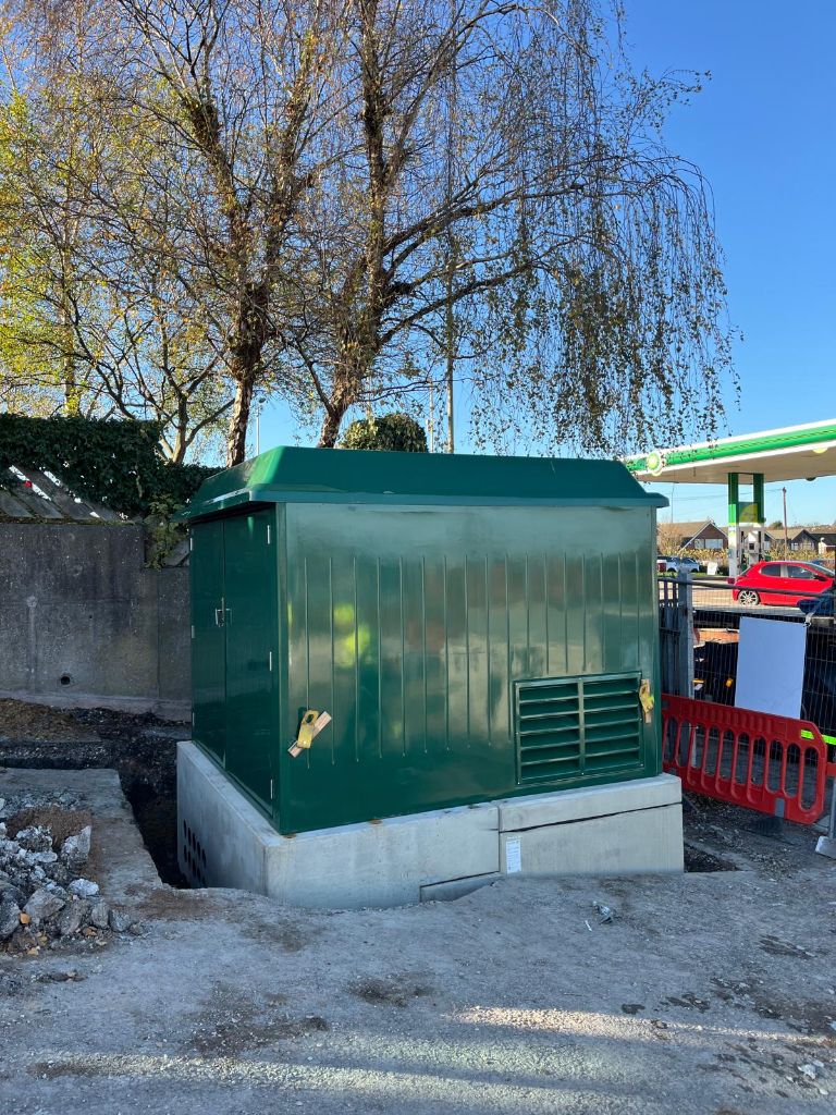 Completed green substation kiosk closed and installed on its concrete plinth at the Coseley hub site — BP petrol station forecourt visible behind